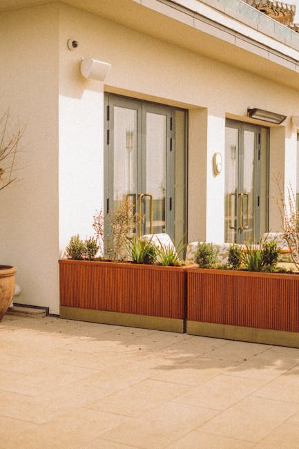 A small, neatly maintained front garden in a residential area with a white-painted boundary wall and a paved pathway leading to a light blue front door, displaying the house number 78. The garden feat